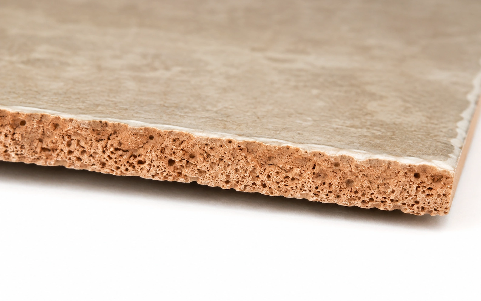 Close up of a ceramic floor tile edge showing a thin glaze over a porous reddish clay bisque body