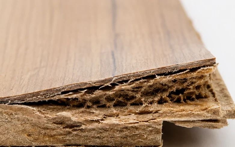 Close up of a standard laminate flooring plank edge with a swollen, delaminated fiberboard core after water damage