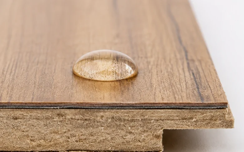Close up of a water resistant laminate flooring plank edge with a bead of water sitting on the sealed surface