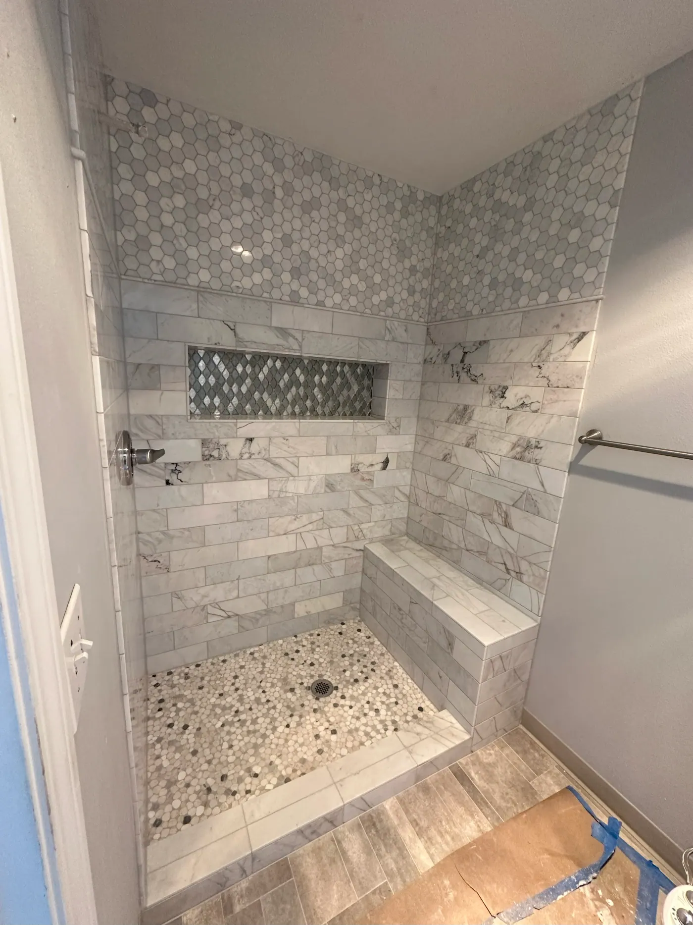 Marble tile shower with a bench and pebble mosaic floor in a Tulsa metro home